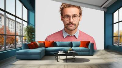 Serious male teacher with confident clever look, has beard and mustache, listens pupil`s answer, wears pink sweater, round glasses, isolated over white background. People, facial expressions concept Wall mural